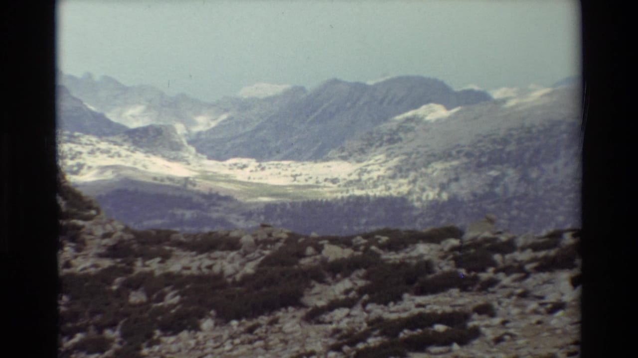 Wide mountain valley with snow-patched peaks and rocky alpine foreground.