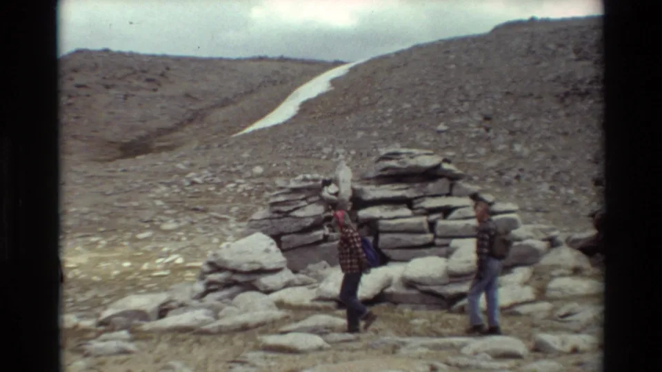 Two backpacked hikers pass a stacked stone cairn in the metadata-supported 1981 mountain hiking scene.
