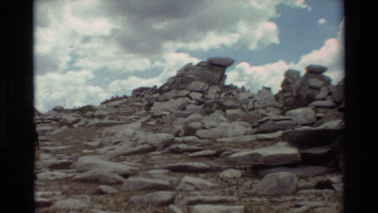 1981 8mm frame of a rugged rocky slope with layered boulders and clouds overhead, location supplied as British Columbia.