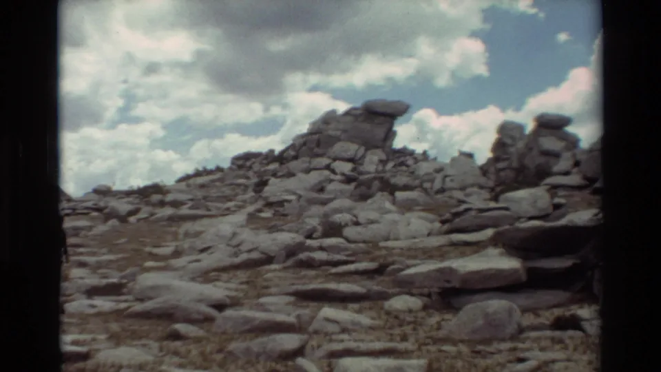 1981 8mm frame of a rugged rocky slope with layered boulders and clouds overhead, location supplied as British Columbia.