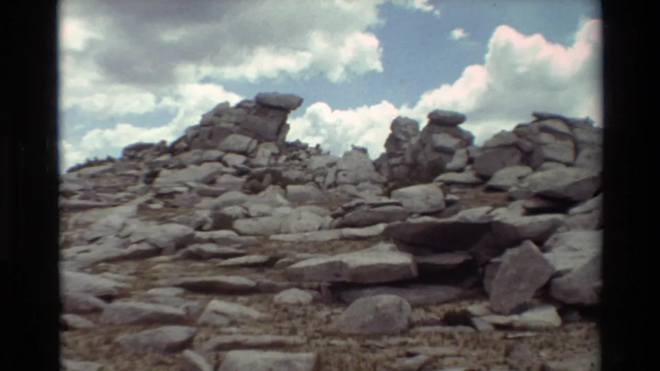 Rocky mountain terrain with stacked boulders and a cloudy sky in supplied 1981 British Columbia home-movie footage.