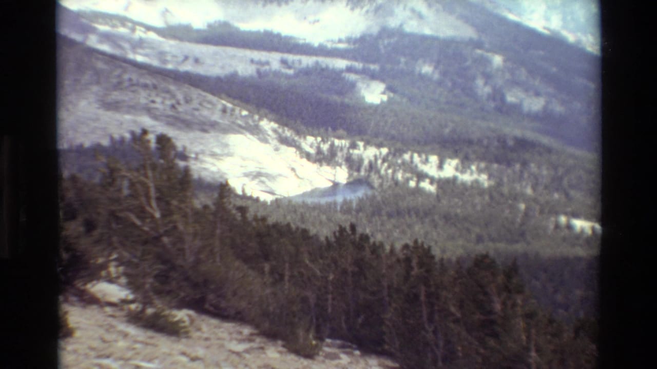 1981 8mm frame showing a snow-dusted alpine valley, evergreen forest, and distant ridgelines in the reported British Columbia sequence.
