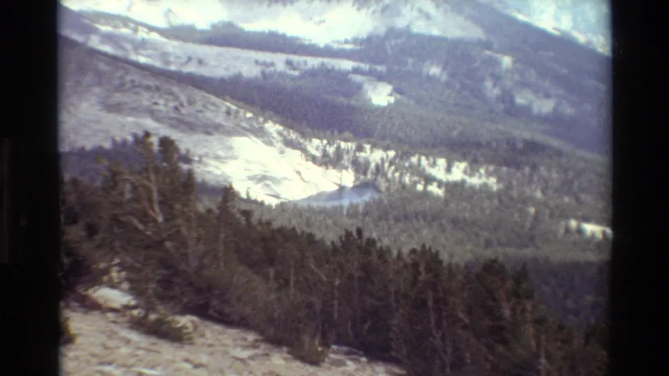 1981 8mm frame showing a snow-dusted alpine valley, evergreen forest, and distant ridgelines in the reported British Columbia sequence.