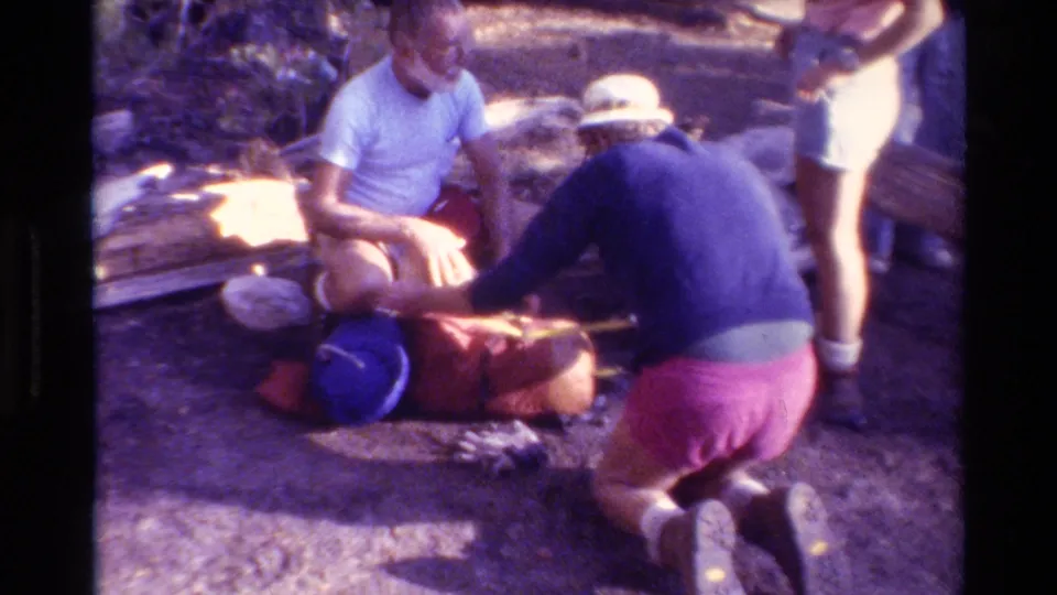 Adults prepare hiking equipment on a forest floor in 1981 British Columbia home-movie footage.