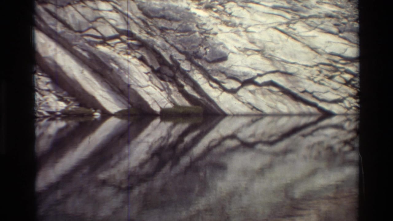 Fractured gray cliff reflected in calm water with soft 8mm frame edges.