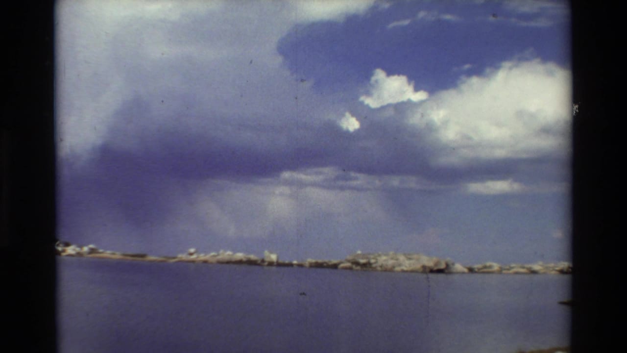Wide lake view with distant rocks and heavy clouds stretching across the sky.