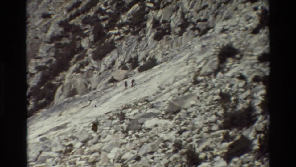 Two distant hikers appear on a pale trail across the rocky slope, emphasizing scale in the 1981 8mm mountain scene.