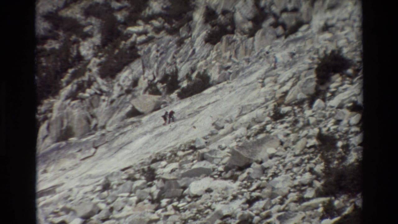 Distant hikers climb across exposed mountain rock in a grainy 1981 8mm travel shot from the listed British Columbia location.