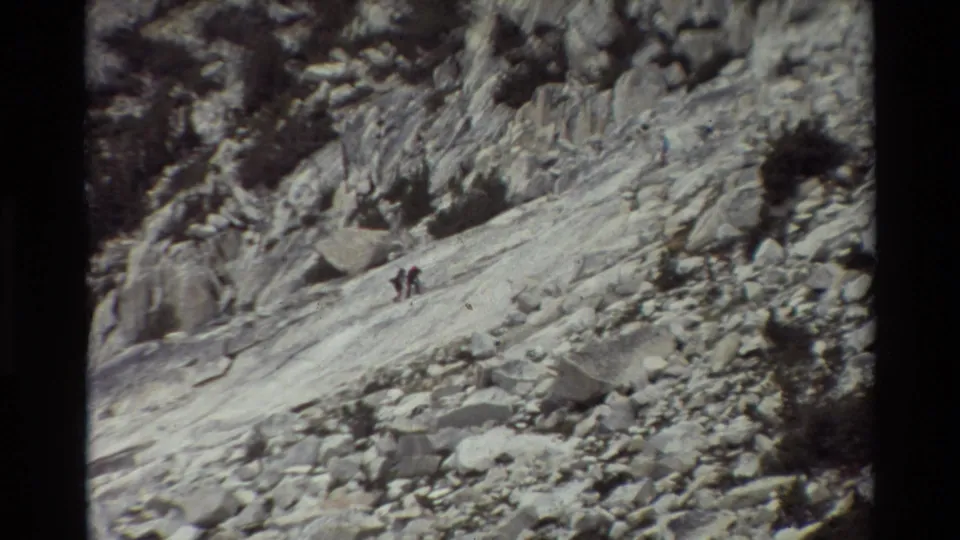 Distant hikers climb across exposed mountain rock in a grainy 1981 8mm travel shot from the listed British Columbia location.