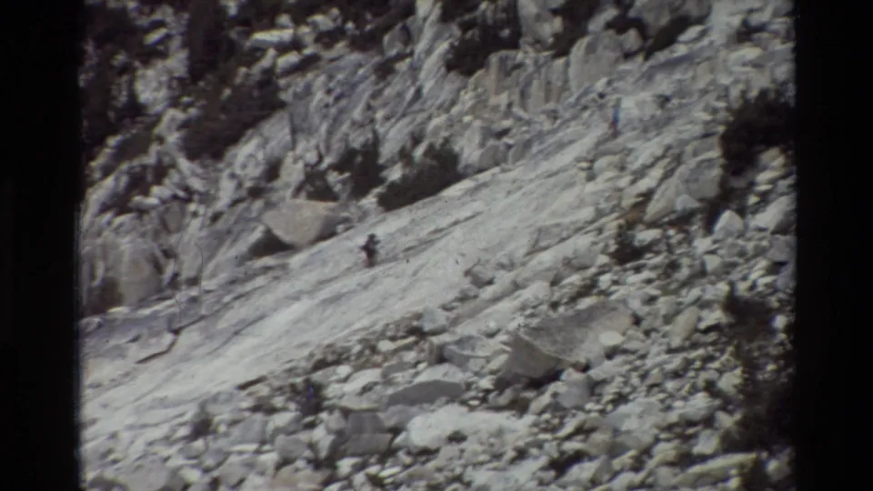 One hiker is most apparent in this 1981 8mm frame, moving along a steep rocky slope while another figure is unclear or out of view.