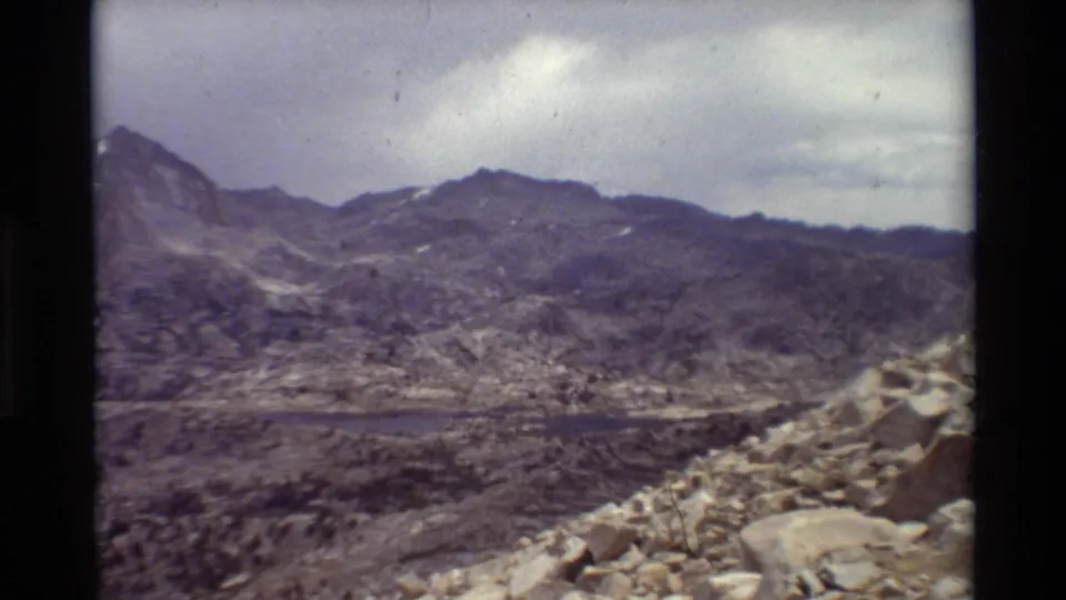A wide mountain panorama shows rocky terrain, a distant lake, and cloudy sky at the end of the 1981 archival clip.