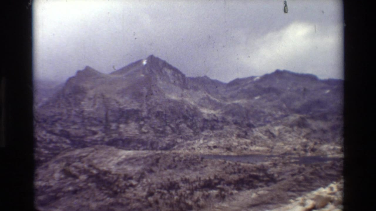 Mountain ridge and lake seen across a rocky valley under clouds.