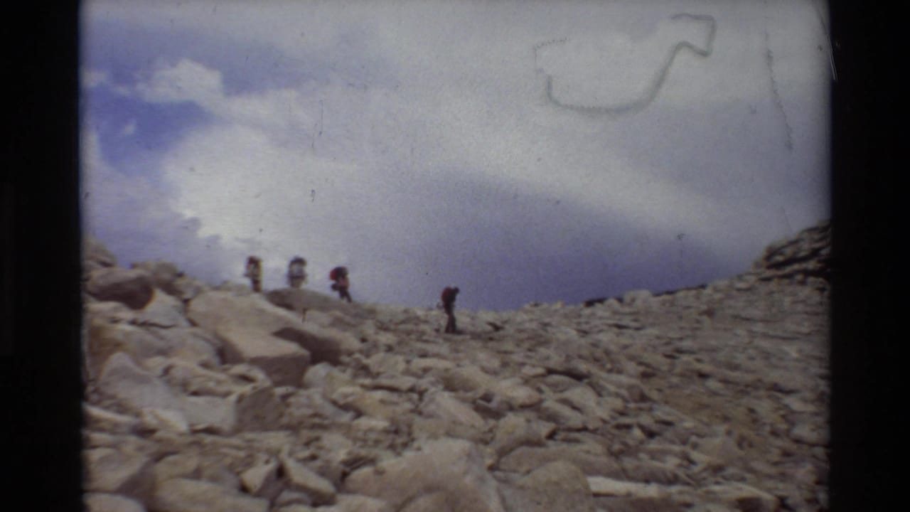 Distant backpackers appear on a rugged rocky slope in archival 8mm footage listed as 1981 British Columbia/USA.