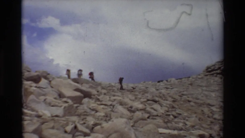 Distant backpackers appear on a rugged rocky slope in archival 8mm footage listed as 1981 British Columbia/USA.