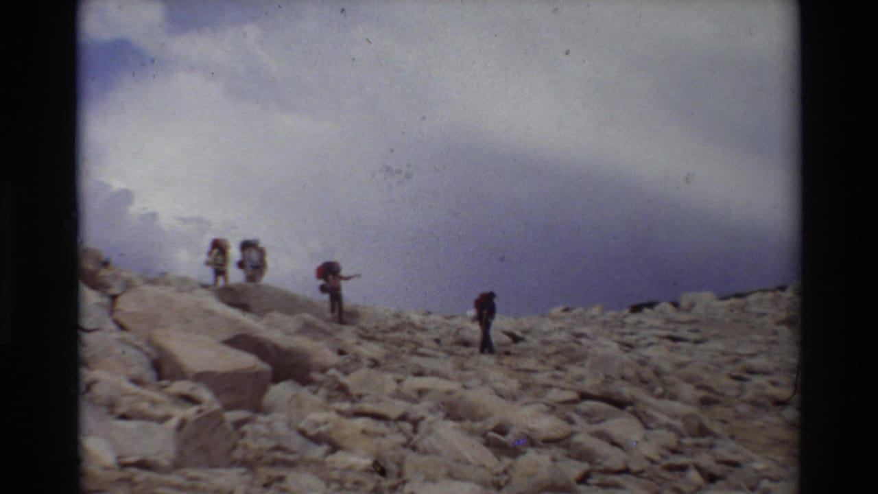 Small group of backpackers walking over uneven rocks on a mountain slope.
