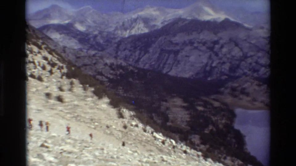 A final 1981 8mm frame shows hikers on the rocky slope, distant ridges, and a partial lake at the valley edge.