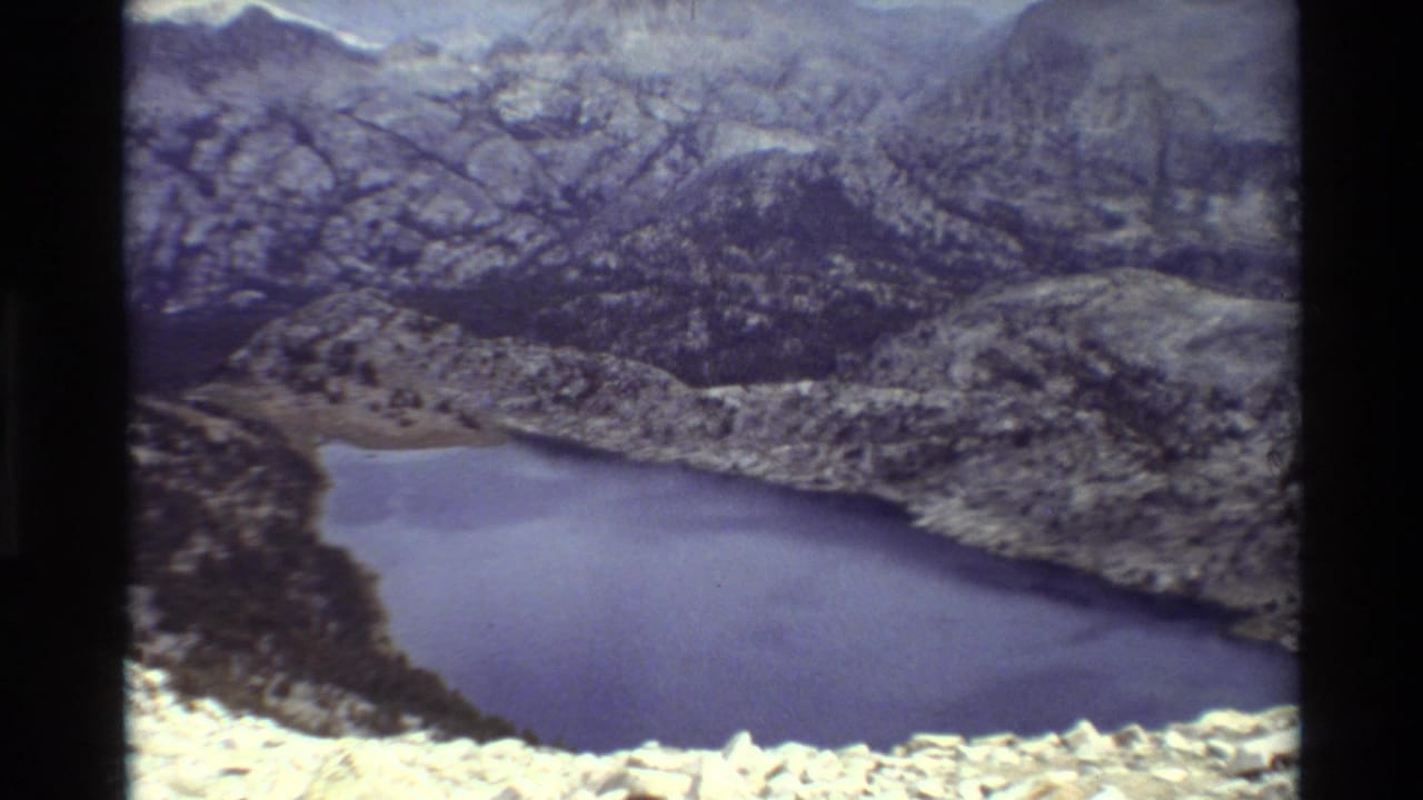 Blue alpine lake below rocky mountain slopes with dark film borders.