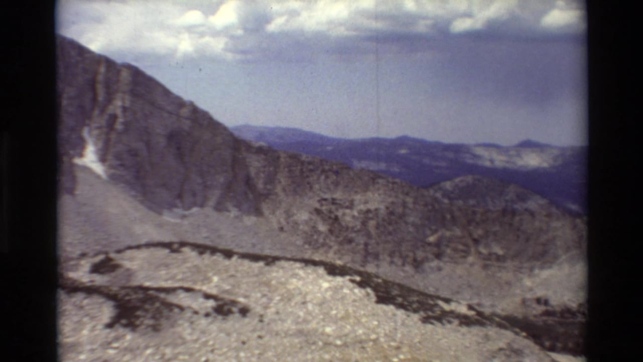 Rocky ridge and distant mountain tops beneath clouds.