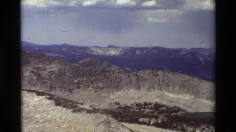Final 8mm frame of the pan showing layered mountain ridges, rocky slopes, cloud cover, and visible film-frame borders.
