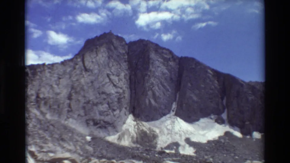 1981 home-movie frame of an alpine rock wall and scree field in British Columbia, with faded color and visible film grain.