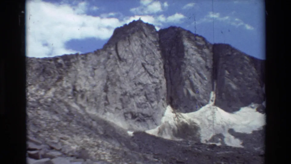 The shot widens to a rugged mountain face with snow patches and blue sky, matching the supplied 1981 outdoor home-movie context.