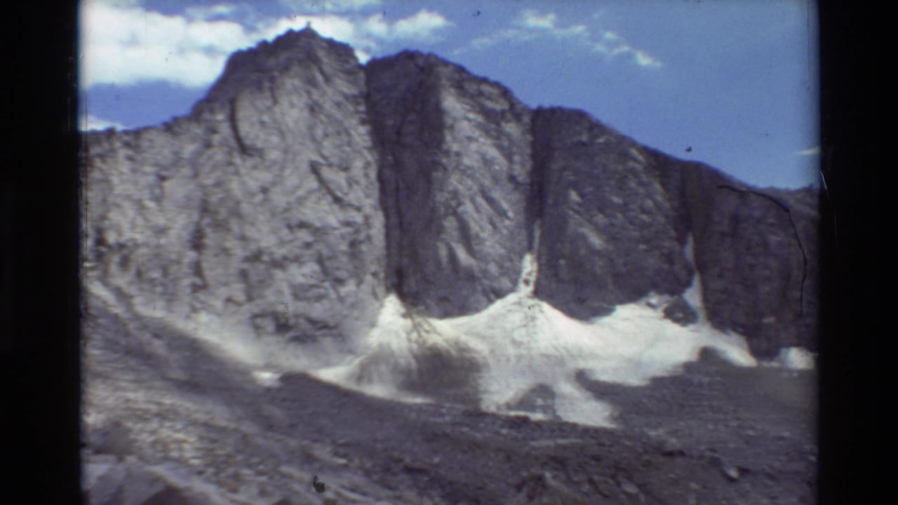 1981 8mm home-movie frame of steep rocky cliffs with snow patches and a pale blue sky, identified by metadata as British Columbia.