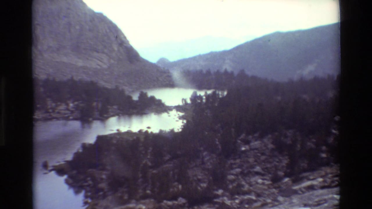Mountain lake between dark evergreen slopes and distant ridges.