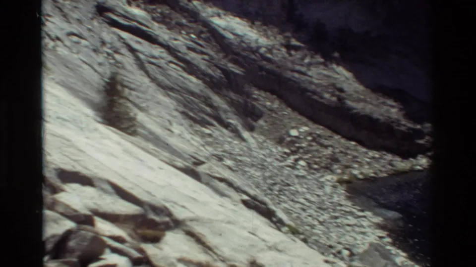 Handheld 8mm view of pale mountain rock, scree, and a small tree on a steep slope in the stated British Columbia-labeled location.