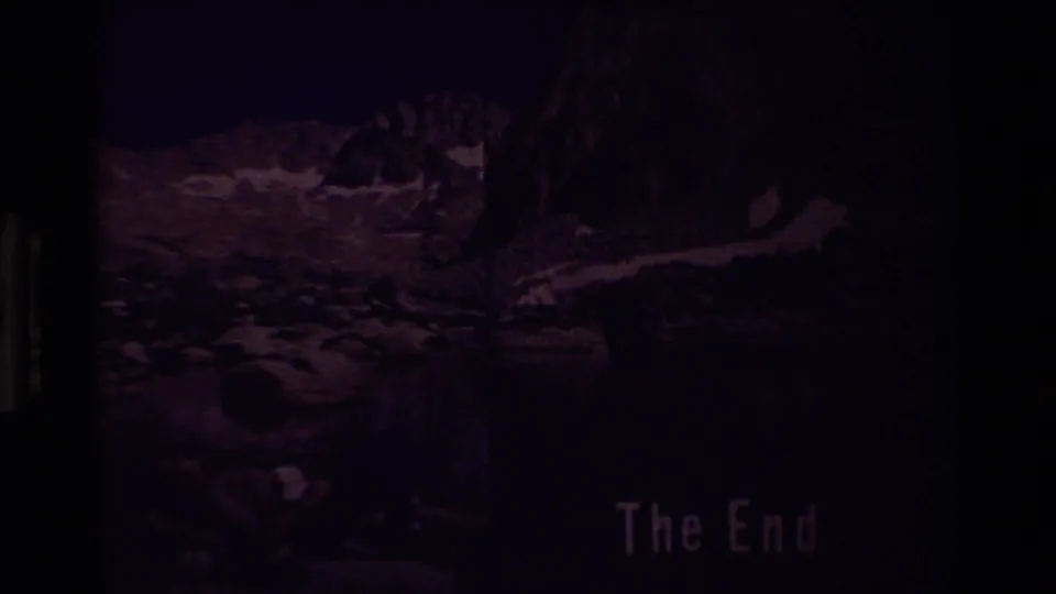 Underexposed 8mm frame of a rocky mountain lake scene with a faint The End title near the lower right.
