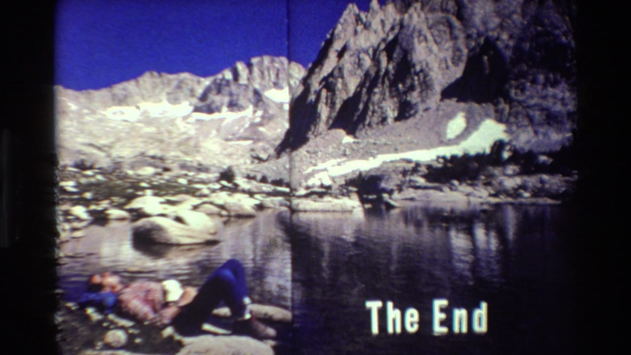 Hiker reclining on rocks beside a mountain lake with a white 'The End' title.