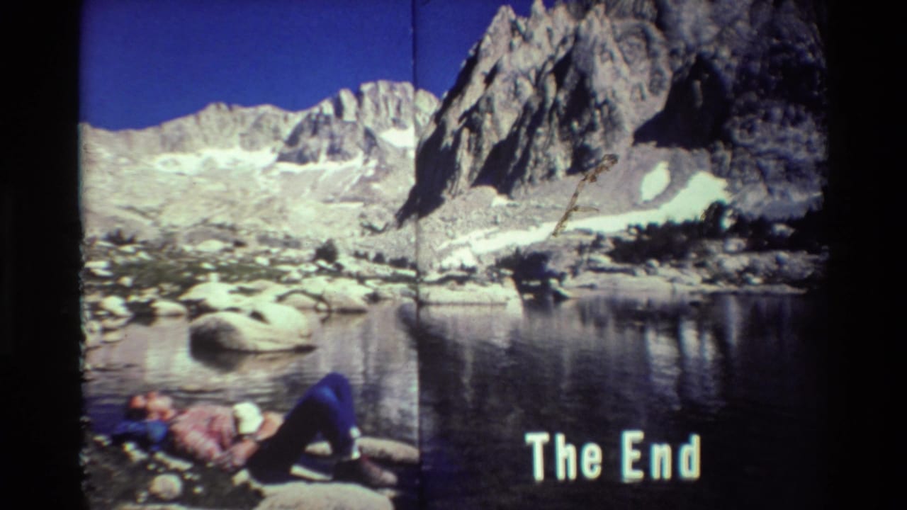 8mm home-movie frame showing a hiker on lakeside rocks below rugged mountains, with 'The End' text over the lower right.