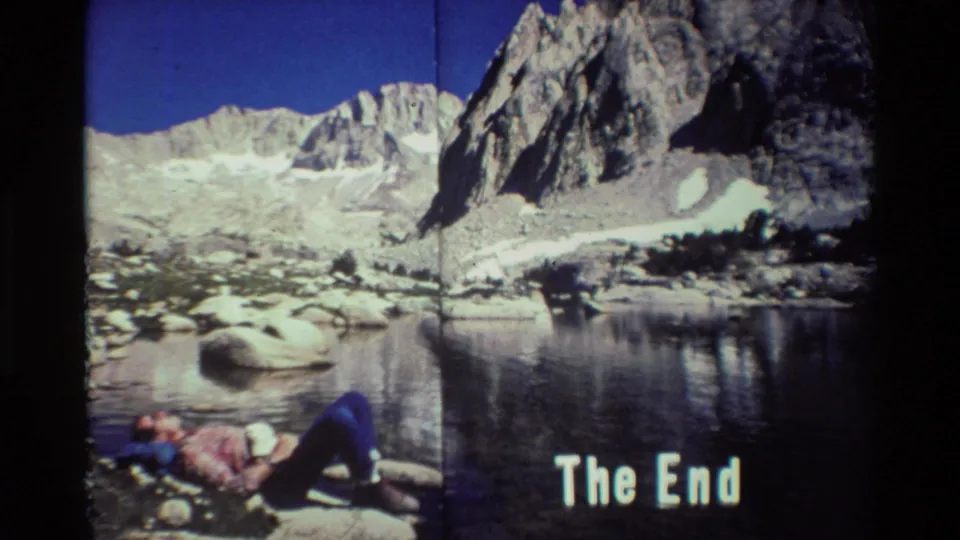 1981 mountain-lake home-movie frame with a resting hiker in the foreground and a white 'The End' title near the bottom.