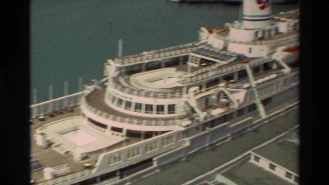 1981 Hawaii home-movie frame looking down at a docked white cruise ship with decks and railings beside harbor water.