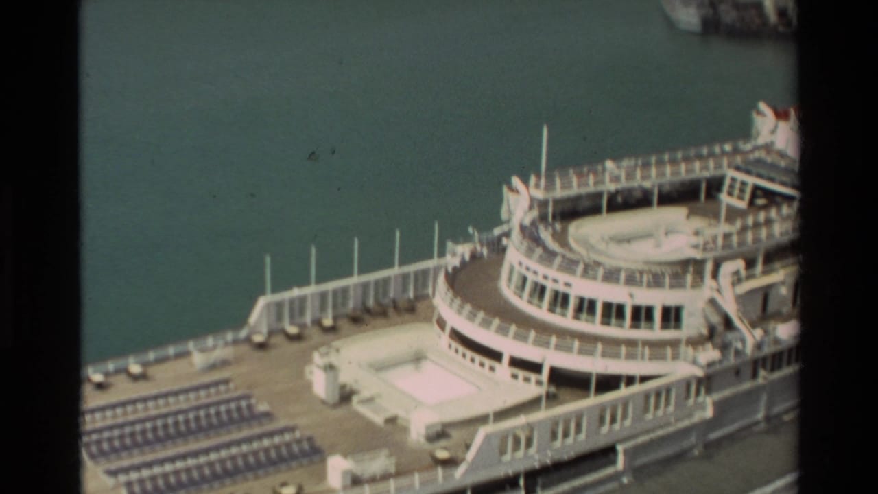 Upper decks of a docked cruise ship with rows of lounge chairs near the water.
