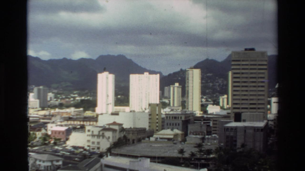 Similar skyline view with white towers, darker office building, and mountains behind the city.