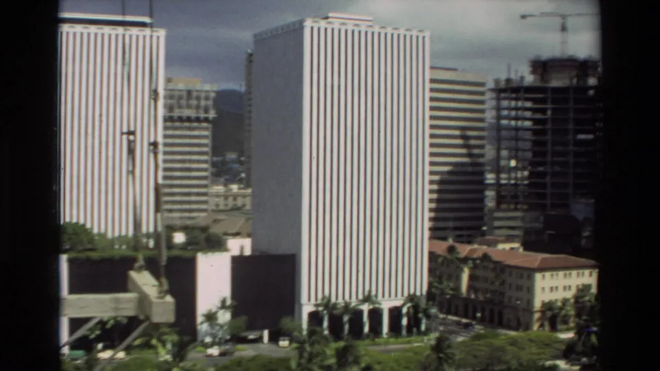 1981 Hawaii urban detail with striped towers, construction crane, unfinished building, and palms near the street level.