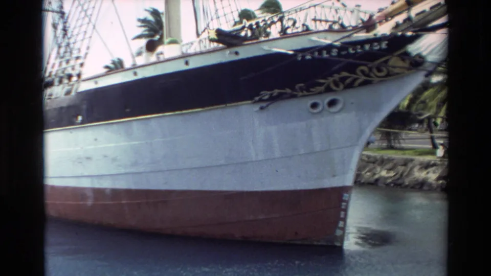 Close 1981 Hawaii view of the Falls of Clyde bow, with rigging, decorative bow detail, dark upper stripe, pale hull, and red waterline.