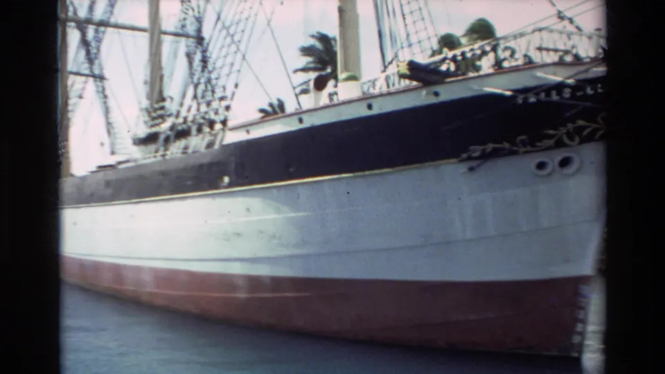 Tighter 1981 Hawaii home-movie view of the Falls of Clyde bow and hull, emphasizing the ship name, rigging, pale side, and red lower hull.