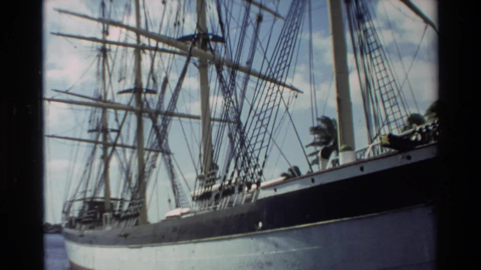 1981 Hawaii 8mm frame looking upward along the docked sailing ship, showing dense rigging, masts, hull edge, sky, and palms.