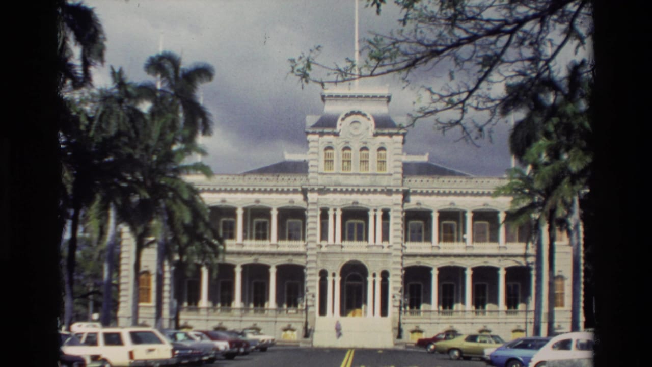 Wide view of an ornate white building behind palm trees and parked cars.