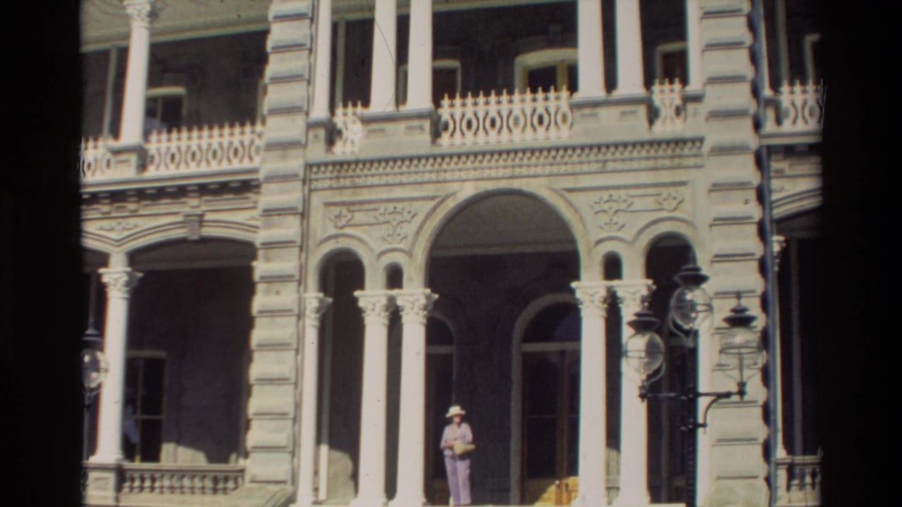 Closer 1981 Hawaii view of the building entrance, with white columns, decorative arches, balcony railings, and an adult figure near the doorway.