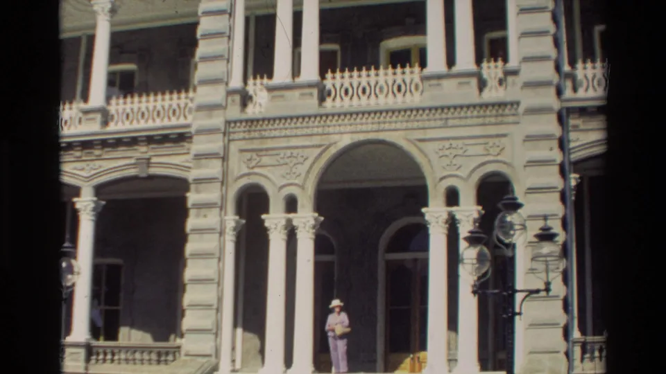 Closer 1981 Hawaii view of the building entrance, with white columns, decorative arches, balcony railings, and an adult figure near the doorway.