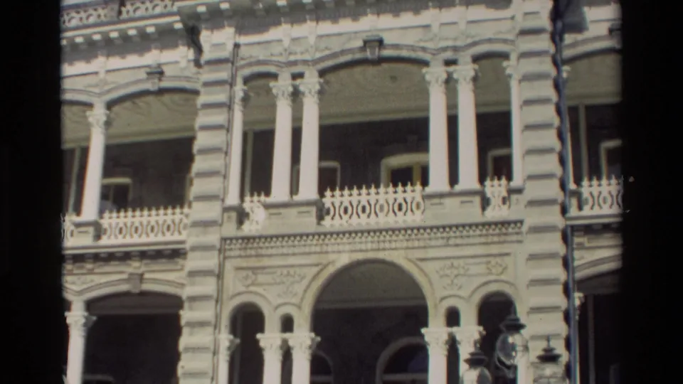 Tight 8mm view of the Hawaii building facade, emphasizing white columns, arched openings, carved details, and upper balcony railings.