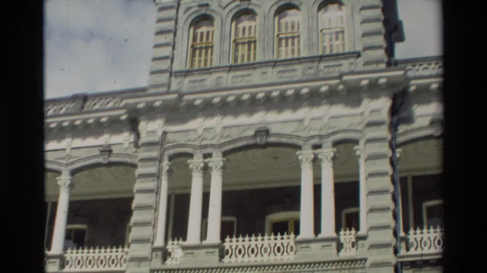 Close 1981 Hawaii frame of the ornate building facade with upper windows, white columns, balcony railings, and decorative exterior molding.