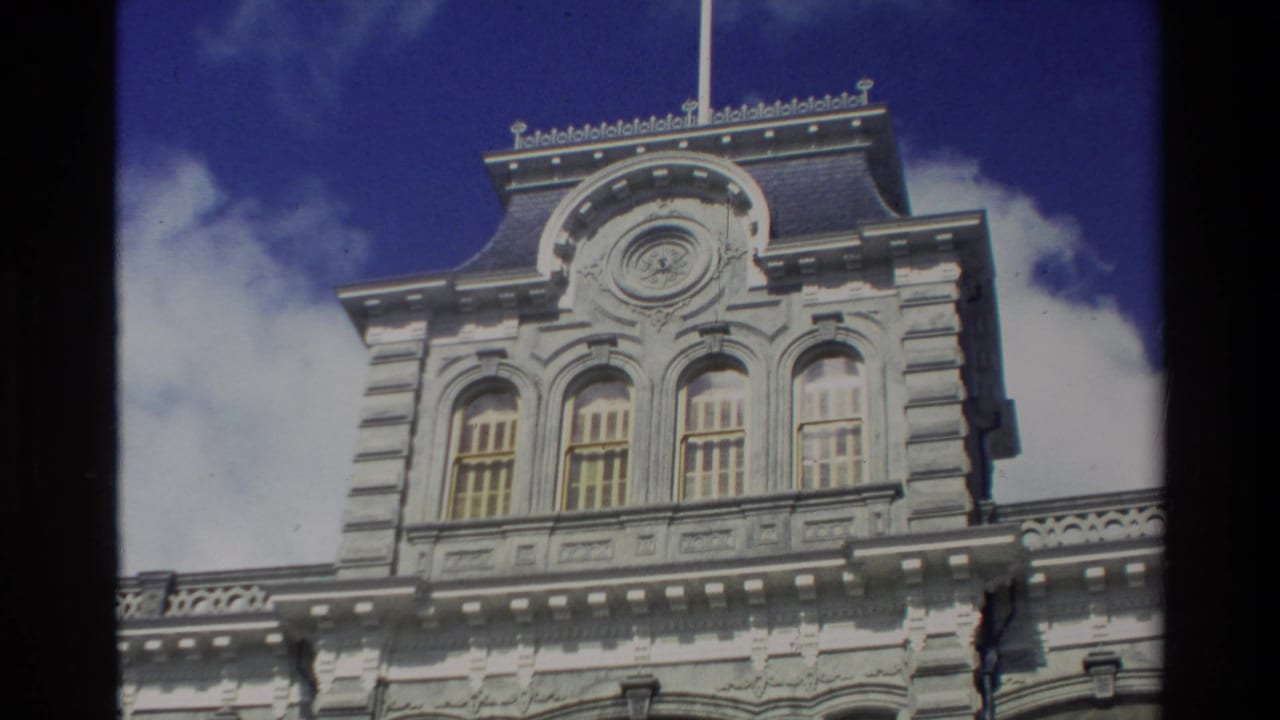 A handheld 1981 Hawaii travel view frames the upper section of a white ornate building against blue sky.