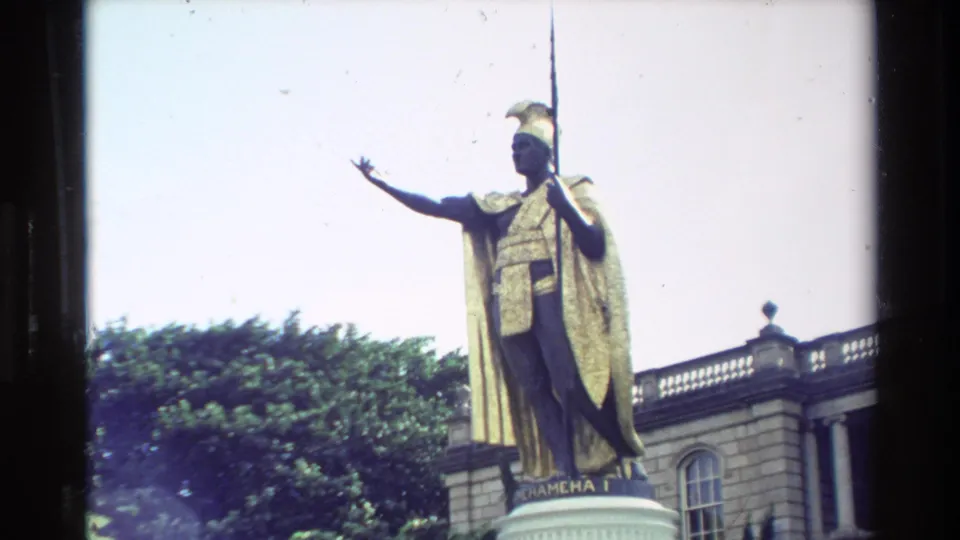 Closer 1981 Hawaii frame of the King Kamehameha I statue, with outstretched arm, spear, cape, trees, and Aliiolani Hale behind.