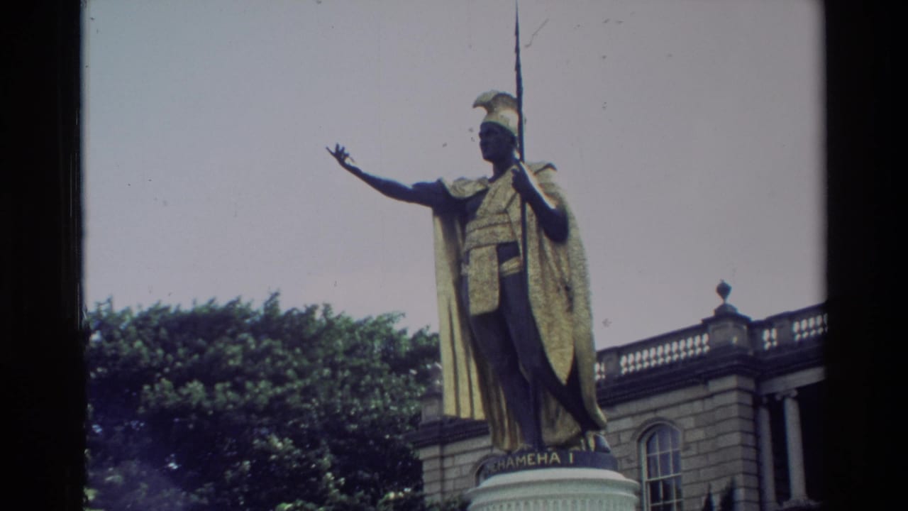 1981 Hawaii home-movie frame showing the King Kamehameha I statue, golden cloak, spear, pedestal, trees, and arched building.