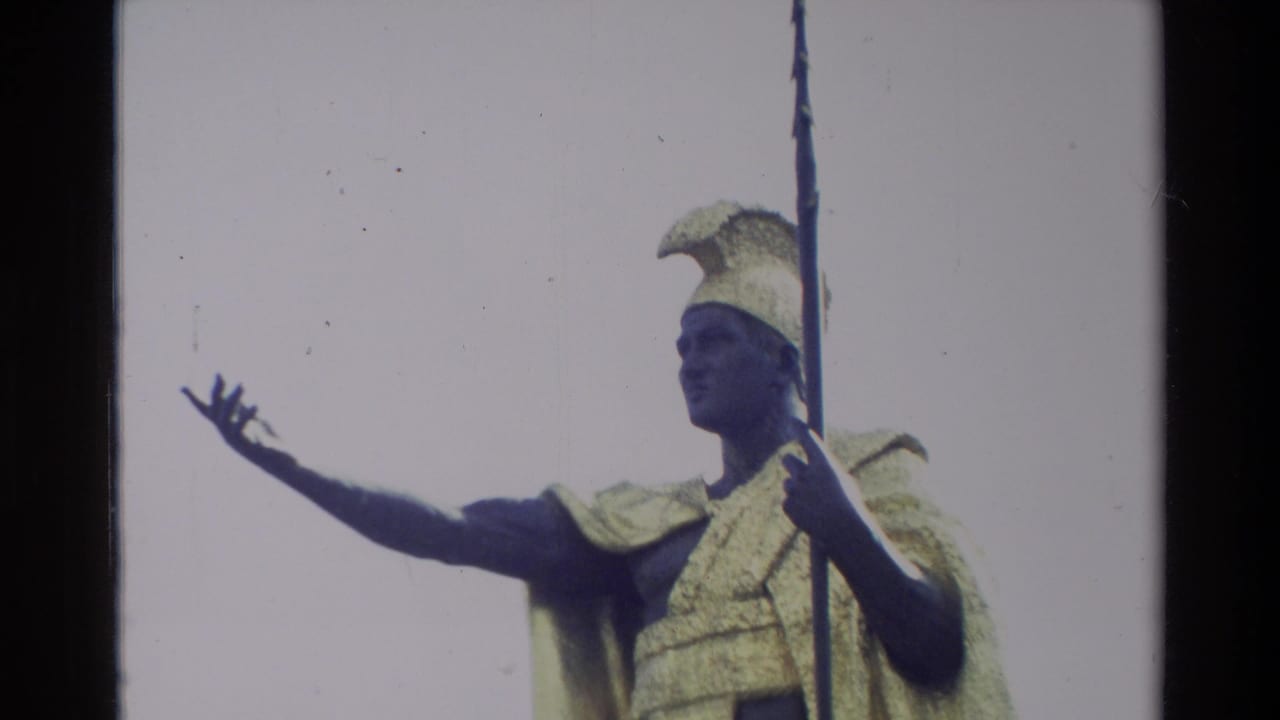 Closer 1981 Hawaii frame of the King Kamehameha I statue with feathered helmet, golden cloak, spear, and extended hand against pale sky.