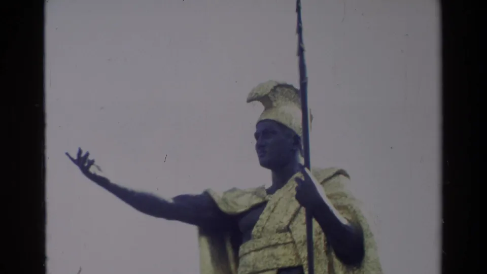 1981 Hawaii 8mm frame with the King Kamehameha I statue cropped close, showing helmet, cloak, spear, and raised open hand.