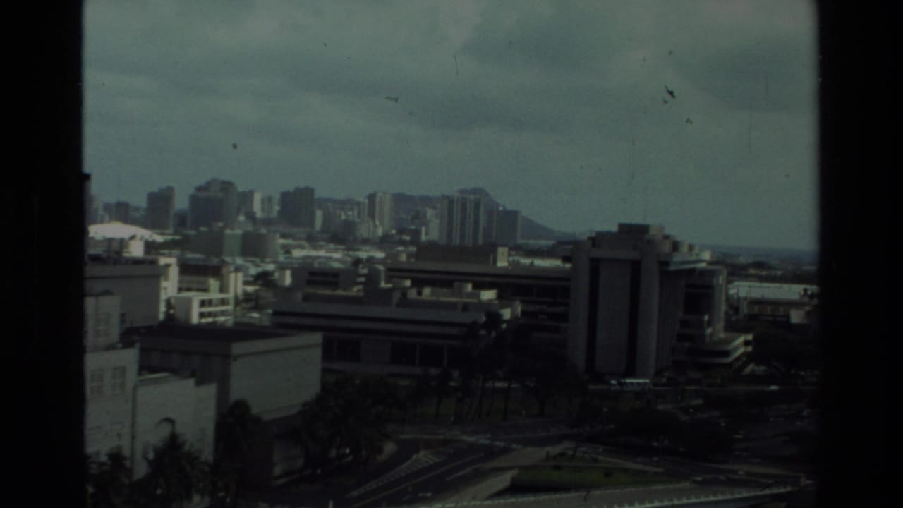 Distant city skyline with Diamond Head beyond low buildings and dark 8mm frame edges.